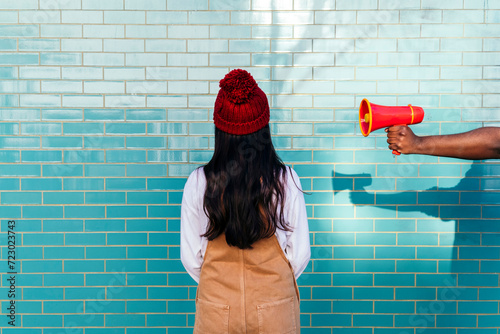 Man's hand holding megaphone by woman facing turquoise brick wall photo