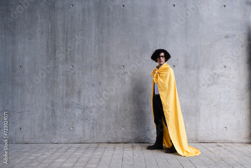 Man wearing yellow cape standing in front of gray wall photo