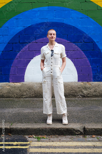 Confident non binary person standing on footpath in front of wall photo