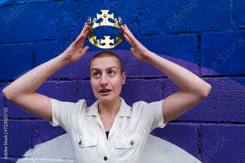 Non-binary person wearing crown in front of colorful wall photo