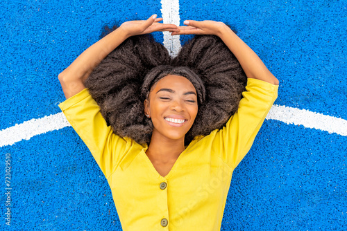 Happy young woman with eyes closed lying on blue basketball court photo