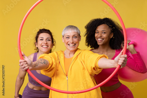 Happy woman with friends holding plastic hoop standing against yellow background