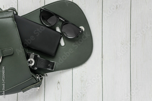 women's accessories on a wooden light background. handbag, glasses, earrings and phone in a black case