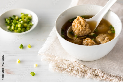 A close up look into a bowl of wonton soup with green onions.