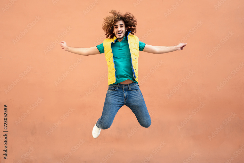 Portrait of smiling young man with curly hair wearing yellow waistcoat jumping in the air Portrait of smiling young man with curly hair wearing yellow waistcoat jumping in the air