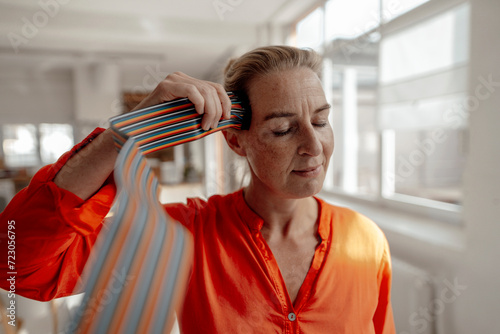 Businesswoman with eyes closed touching computer cables to head at office photo