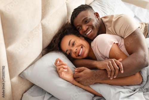 african american couple resting in bedroom together, hugging and smiling
