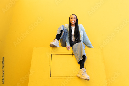Smiling young woman sitting on concrete block near yellow wall photo