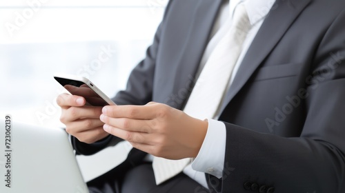 A Close-up of an Asian businesswoman using a mobile phone while working on a laptop computer, white isolated background.