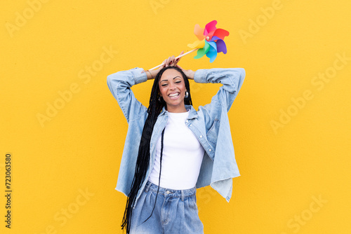 Cheerful woman holding pinwheel toy in front of yellow wall photo
