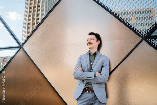 Thoughtful businessman with arms crossed leaning on modern office building photo