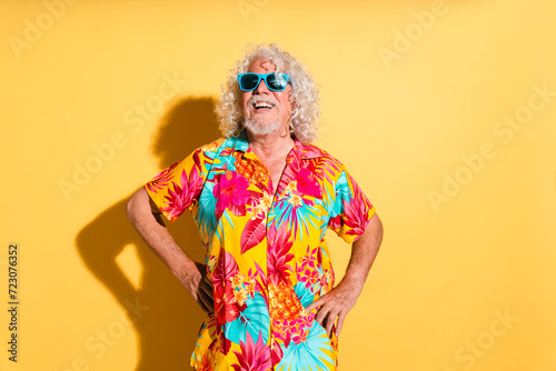 Happy senior man wearing sunglasses and standing with hands on hips against yellow background photo