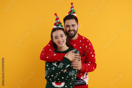 Happy young couple in Christmas sweaters on orange background