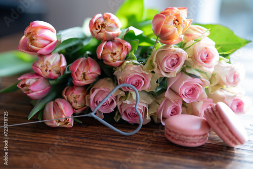 Beautiful bouquet of flowers with sweet delicacies. Heart shape, sweet pastries with pink roses and tulips on wooden table. Background for mother's day and wedding.