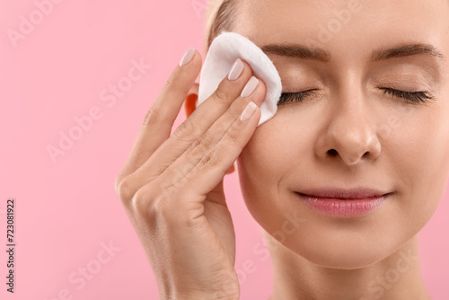 Beautiful woman removing makeup with cotton pad on pink background, closeup. Space for text