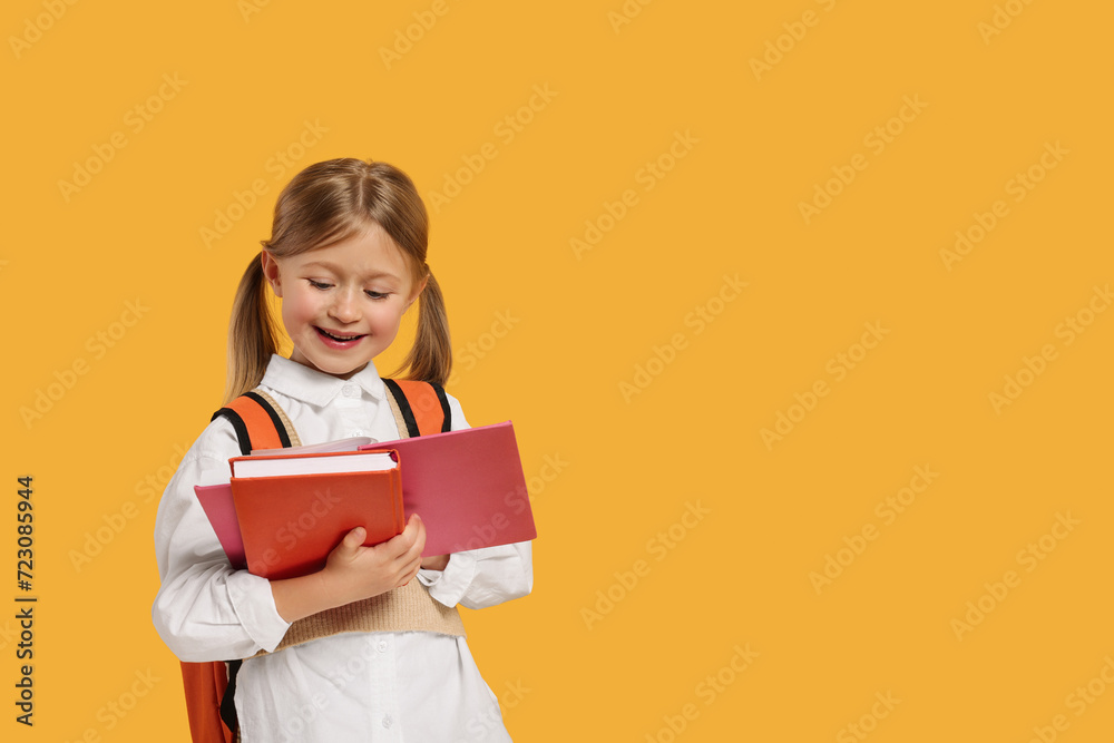 Happy schoolgirl with backpack and books on orange background, space for text Happy schoolgirl with backpack and books on orange background, space for text
