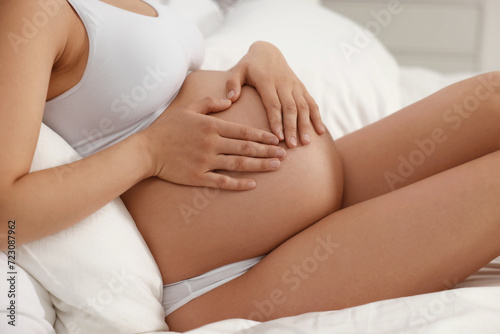 Pregnant woman in stylish comfortable underwear making heart with hands on her belly on bed, closeup
