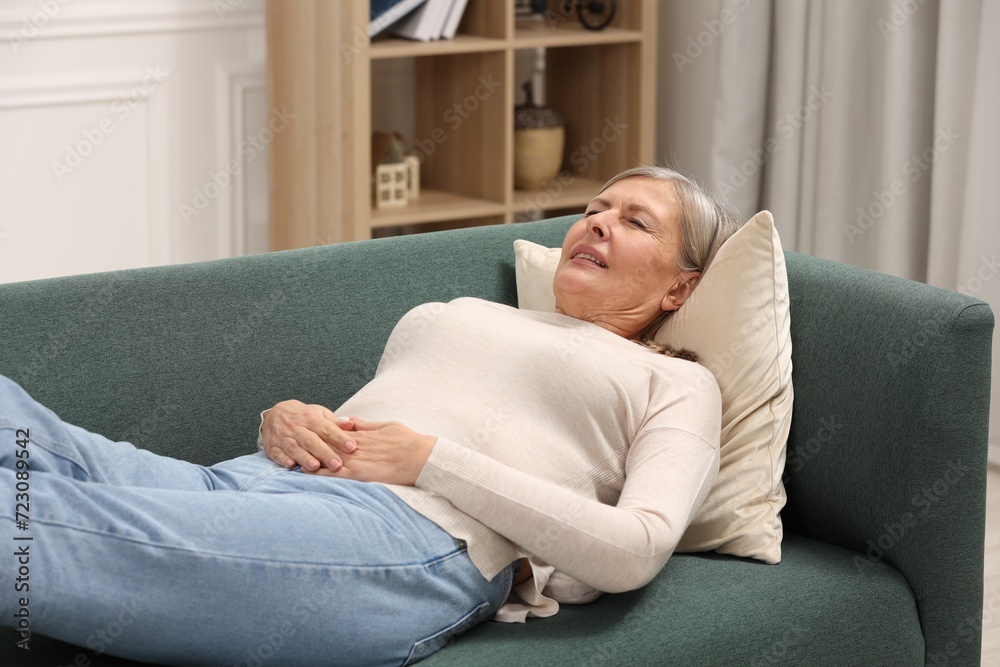 Menopause. Woman suffering from abdominal pain on sofa at home Menopause. Woman suffering from abdominal pain on sofa at home