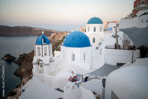 View of Oia white washed buildings with the famous three blue domes church taken at sunrise
