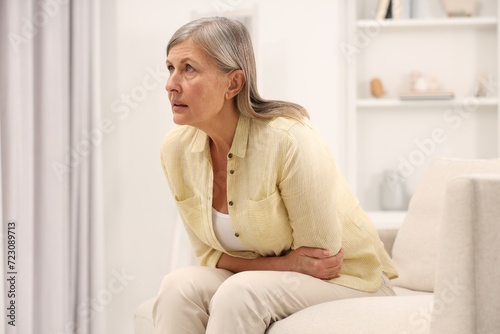 Menopause. Woman suffering from abdominal pain on sofa at home, space for text