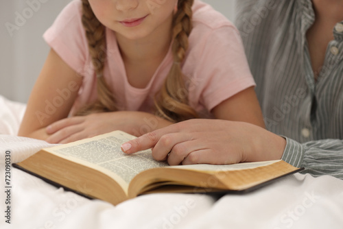 Fotografie Girl and her godparent reading Bible together indoors, closeup
