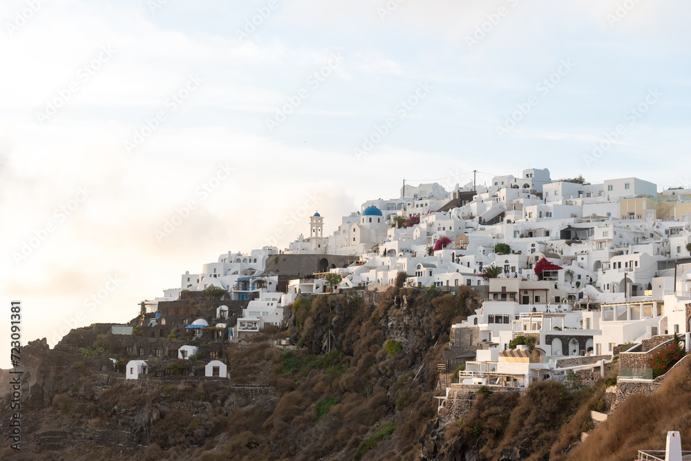 View of Imerovigli village in Santorini with white washed buildings with blue dome church and blue sky