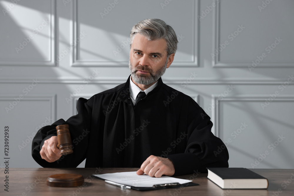 Judge with gavel, papers and book sitting at wooden table indoors Judge with gavel, papers and book sitting at wooden table indoors