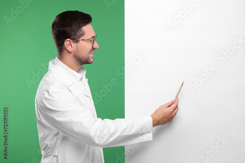 Ophthalmologist pointing at blank banner on green background, space for text photo