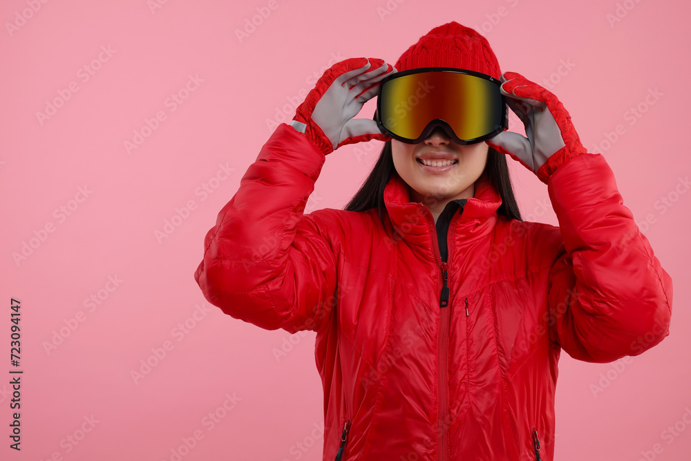 Happy woman in winter sportswear and goggles on pink background. Space for text Happy woman in winter sportswear and goggles on pink background. Space for text
