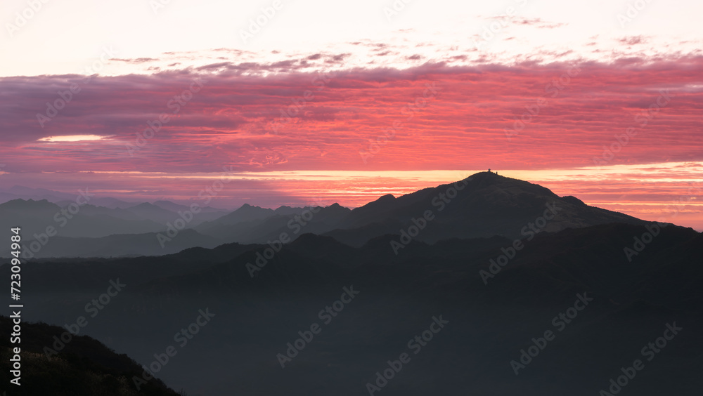 Silhouettes of mountains in golden sunset. Moving clouds in orange sky. Warm winter mountain scenery in northern Taiwan, Shuangxi Buyanting Pavilion.