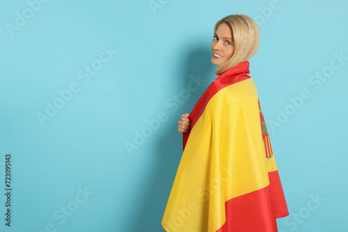 Woman with flag of Spain on light blue background, space for text