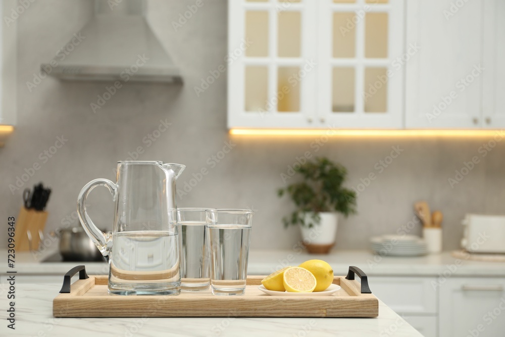 Jug, glasses with clear water and lemons on white table in kitchen, space for text Jug, glasses with clear water and lemons on white table in kitchen, space for text