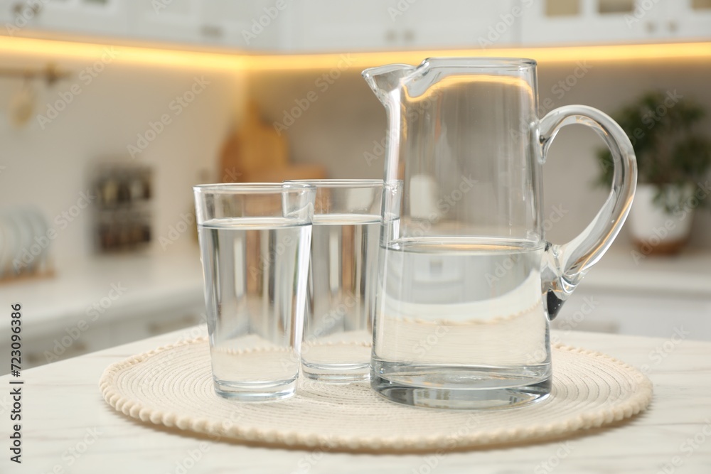 Jug and glasses with clear water on white table in kitchen Jug and glasses with clear water on white table in kitchen