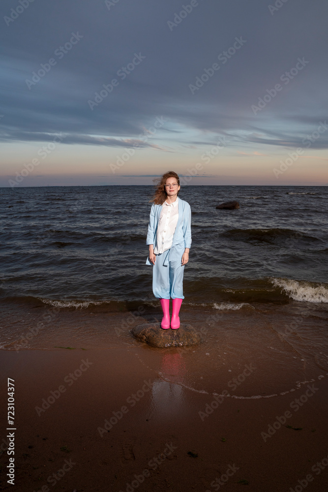 Woman wearing pink rubber boots standing on rock at sunset Woman wearing pink rubber boots standing on rock at sunset