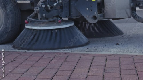 Street sweeper truck with rotating brushes cleaning the sidewalk pavement surface, slow motion