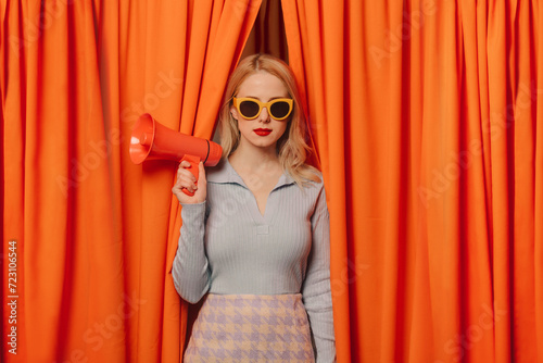 Confident woman holding megaphone standing amidst curtains photo