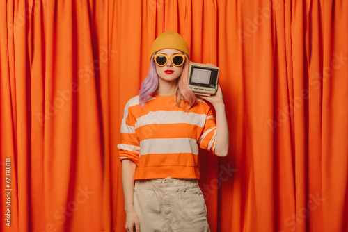 Woman wearing knit hat holding retro style television set in front of orange curtain photo