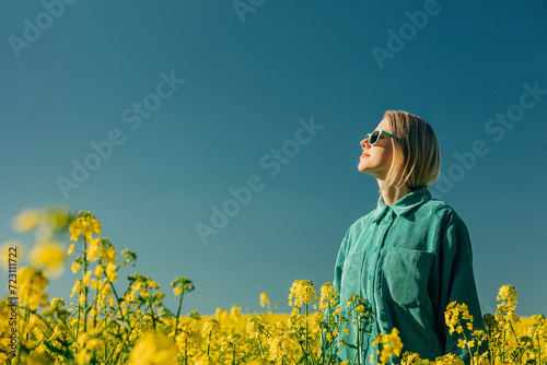 Woman standing amidst flowers in rapeseed field at sunny day photo