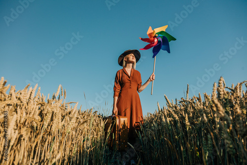 Woman holding suitcase standing with pinwheel toy in wheat field