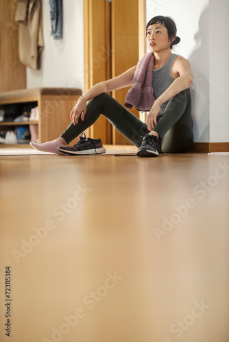 A fit middle-aged fit asian woman sitting on the floor at home and resting from exercises.