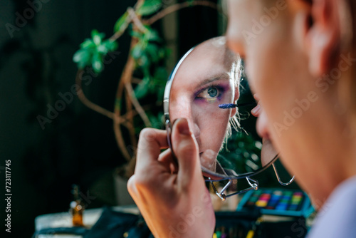 Reflection of man applying mascara in hand mirror photo