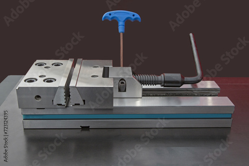 Precision modular vise on metal table black background. Mixed red and white lighting.