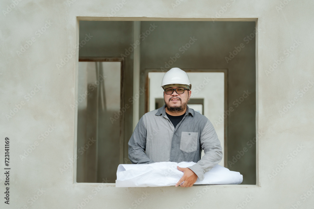 Employee engineer architect designer manager foreman Asian man Standing holding house structural model unfinished window sill wearing white safety helmet prevent things falling. home construction site Employee engineer architect designer manager foreman Asian man Standing holding house structural model unfinished window sill wearing white safety helmet prevent things falling. home construction site