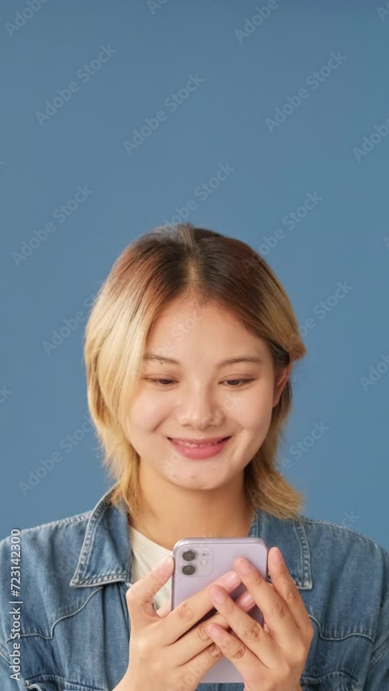 Smiling young woman using mobile phone isolated on blue background Smiling young woman using mobile phone isolated on blue background