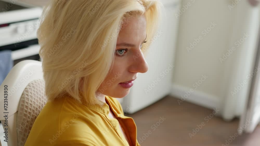 High angle shot of young blond woman talking while sitting on chair in light kitchen. High angle shot of young blond woman talking while sitting on chair in light kitchen.
