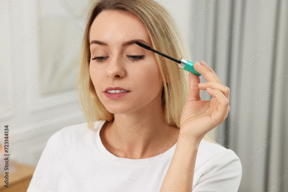 Beautiful woman applying mascara with brush indoors Beautiful woman applying mascara with brush indoors