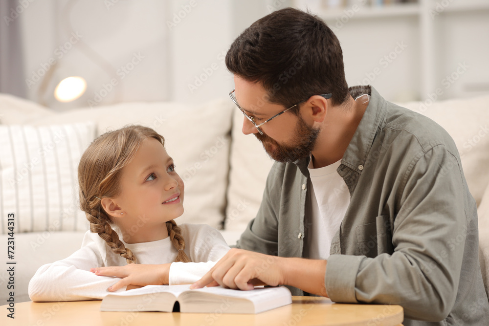 Girl and her godparent reading Bible together at table in room Girl and her godparent reading Bible together at table in room