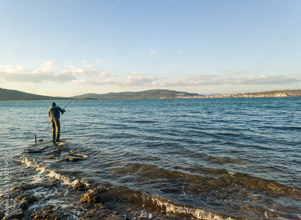 Fishing for pike, perch, carp. Fisherman with rod, spinning reel on sea or ocean. Man catching fish, pulling rod while fishing on sea, pond. Wild nature. The concept of rural getaway. Back view. 