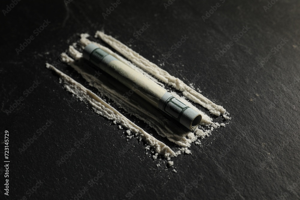 Naklejka premium Drug addiction. Cocaine and rolled dollar banknote on dark textured background, closeup