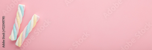Two colorful swirl soft marshmallow candies on light pink table background. Pastel color. Sweet snack closeup. Wide banner. Empty place for text. Top down view.
